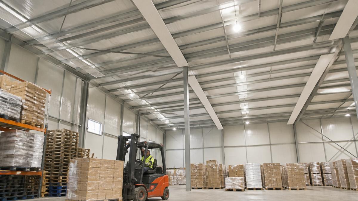 A large warehouse interior with high ceilings, showing infrared radiant heating panels mounted near the roof and a forklift operating below